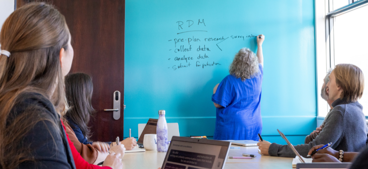 Marjorie at blue board presenting while others take notes